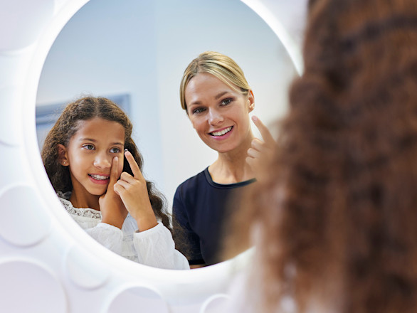 An optician shows a girl how to put in contact lenses