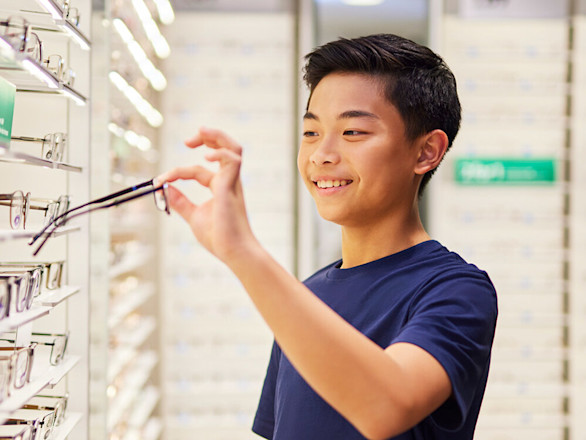 Young boy in blue T-shirt choosing glasses in store.