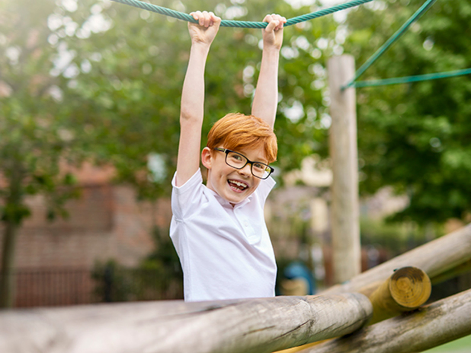 Ginger haired boy in glasses swinging from rope in playground