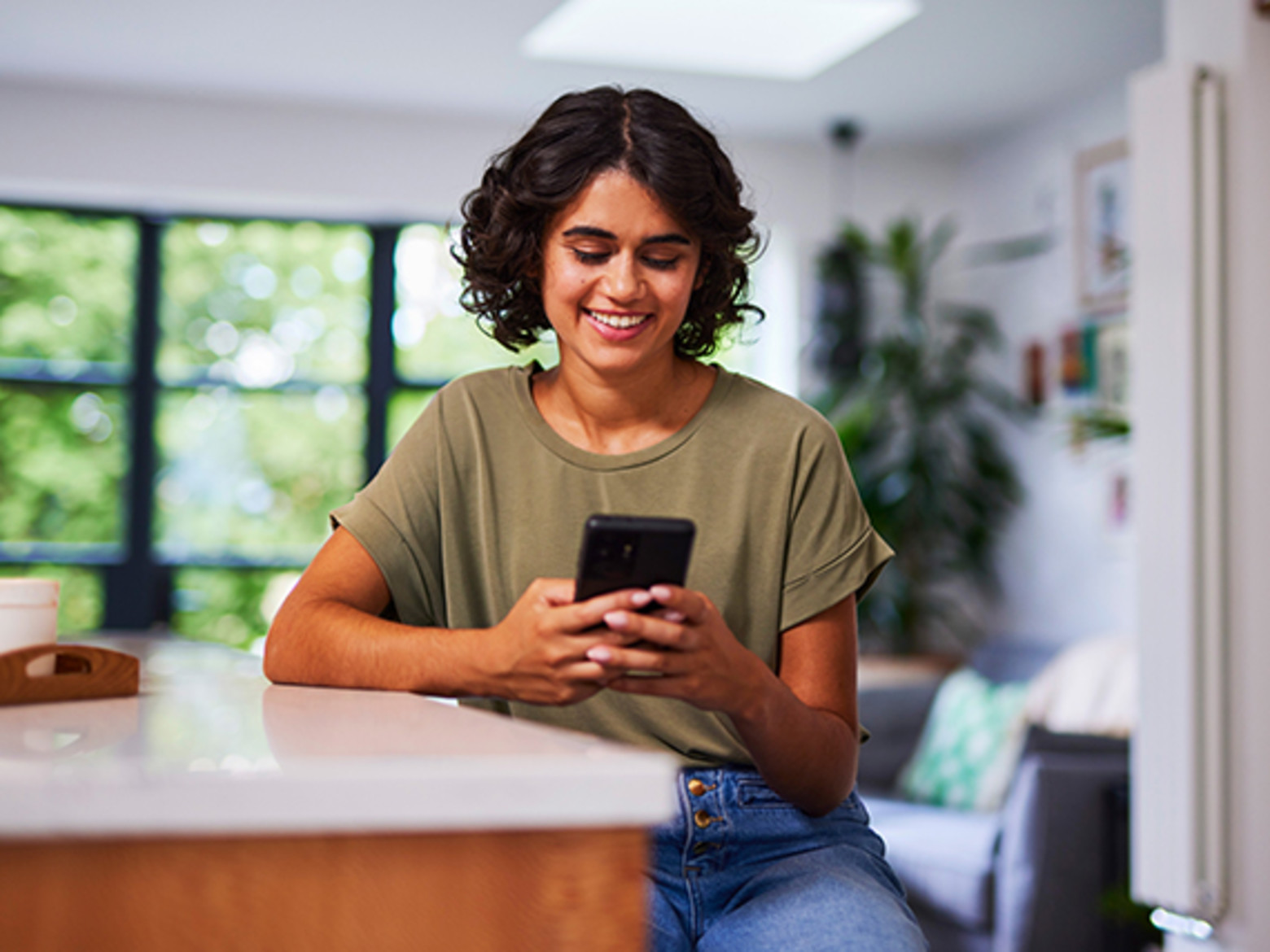 A dark-haired young woman smiling at her mobile phone in her hands