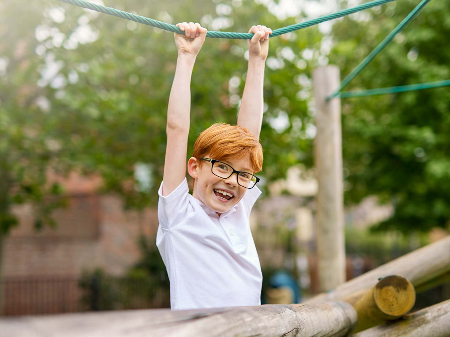 Young boy with red hair and black glasses swinging from a rope