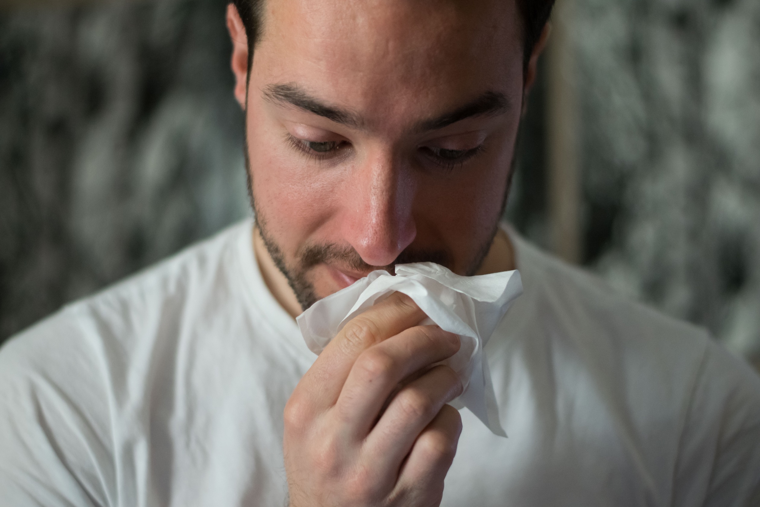 A man holding a tissue to his face while looking downward.