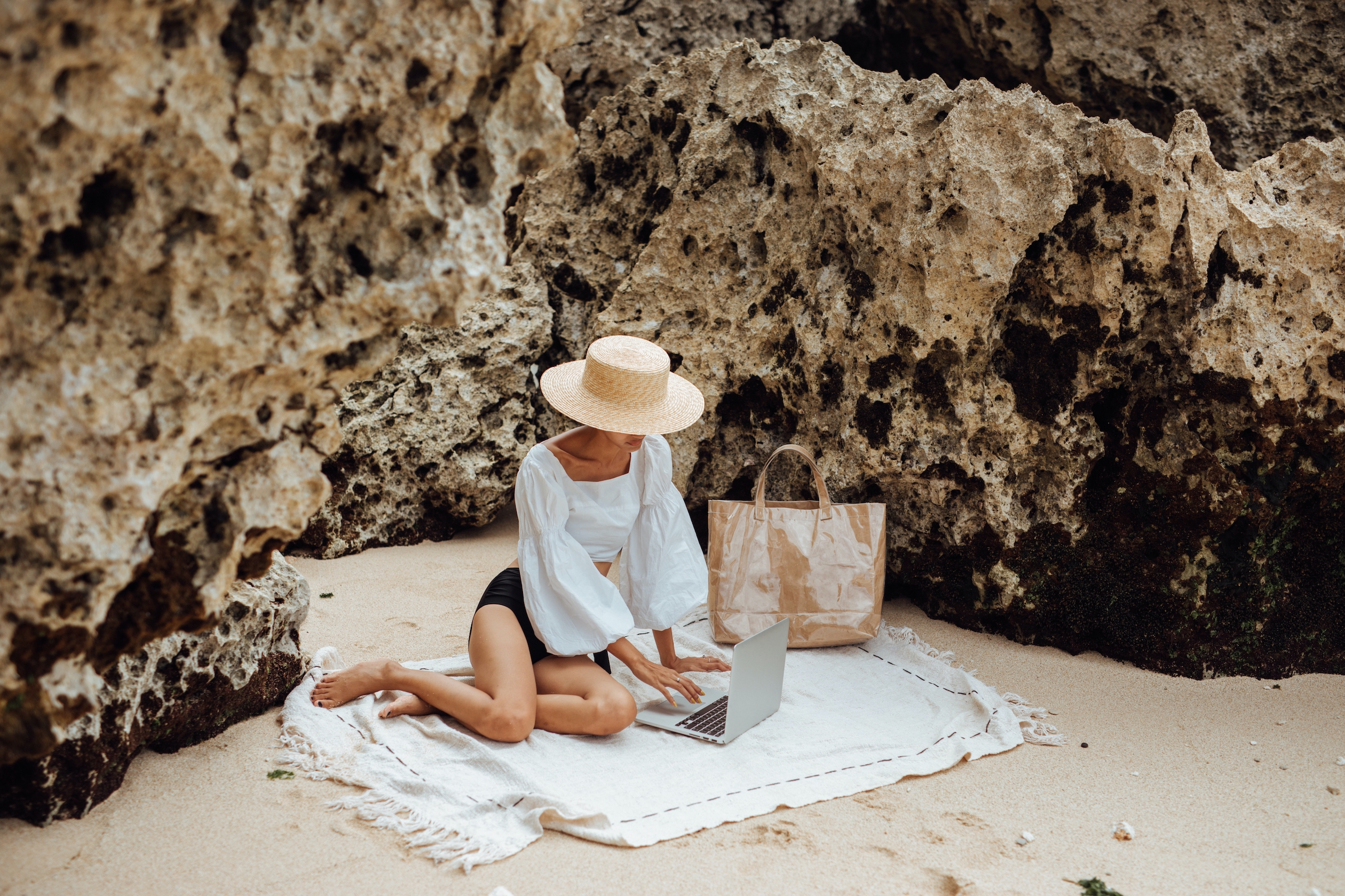 Image of a person reading on their laptop while relaxing at a beach.