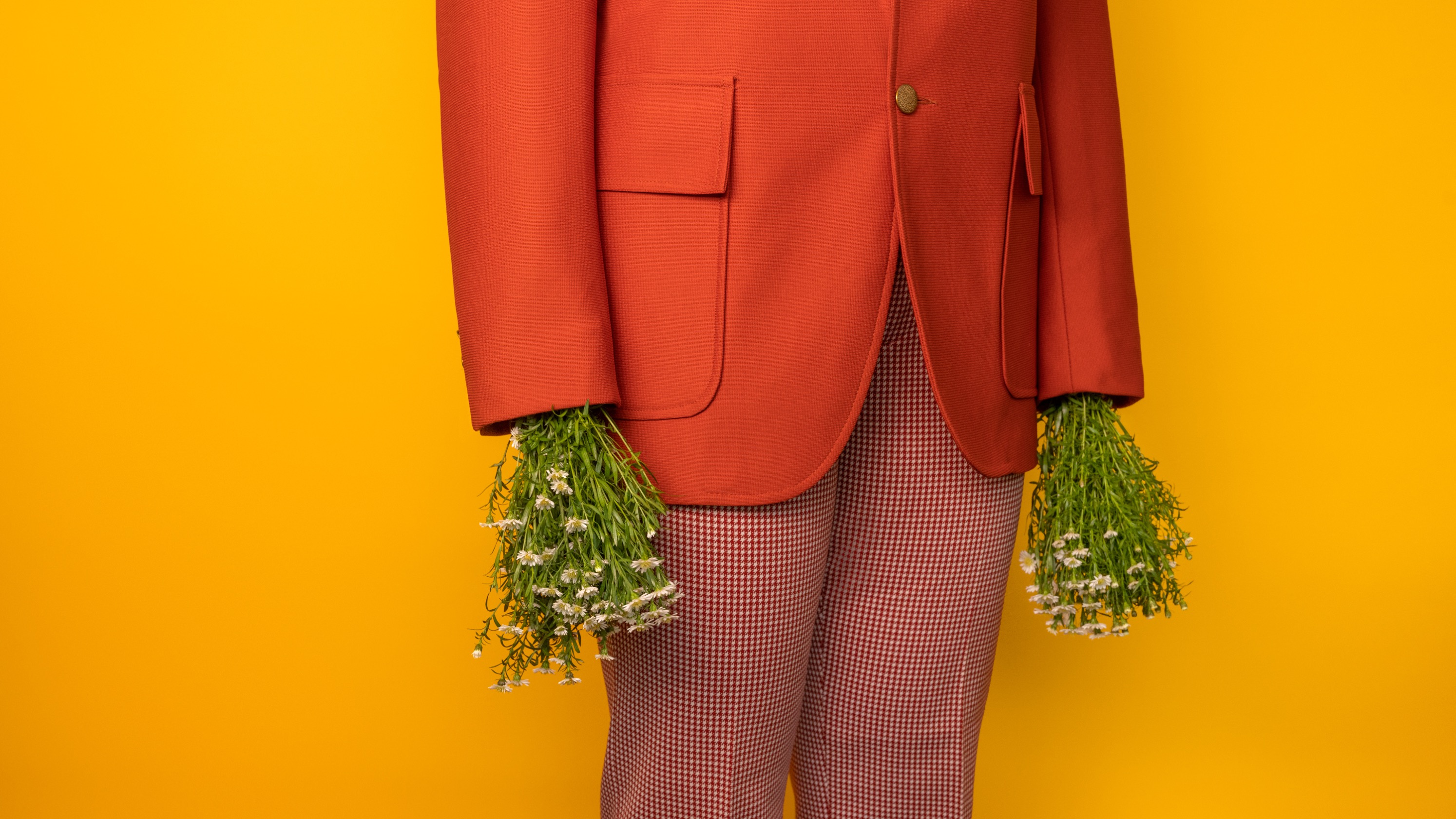 Close-up of a person's torso wearing a brightly-colored suit. Instead of hands, bushels of flowers stick out of the sleeves.
