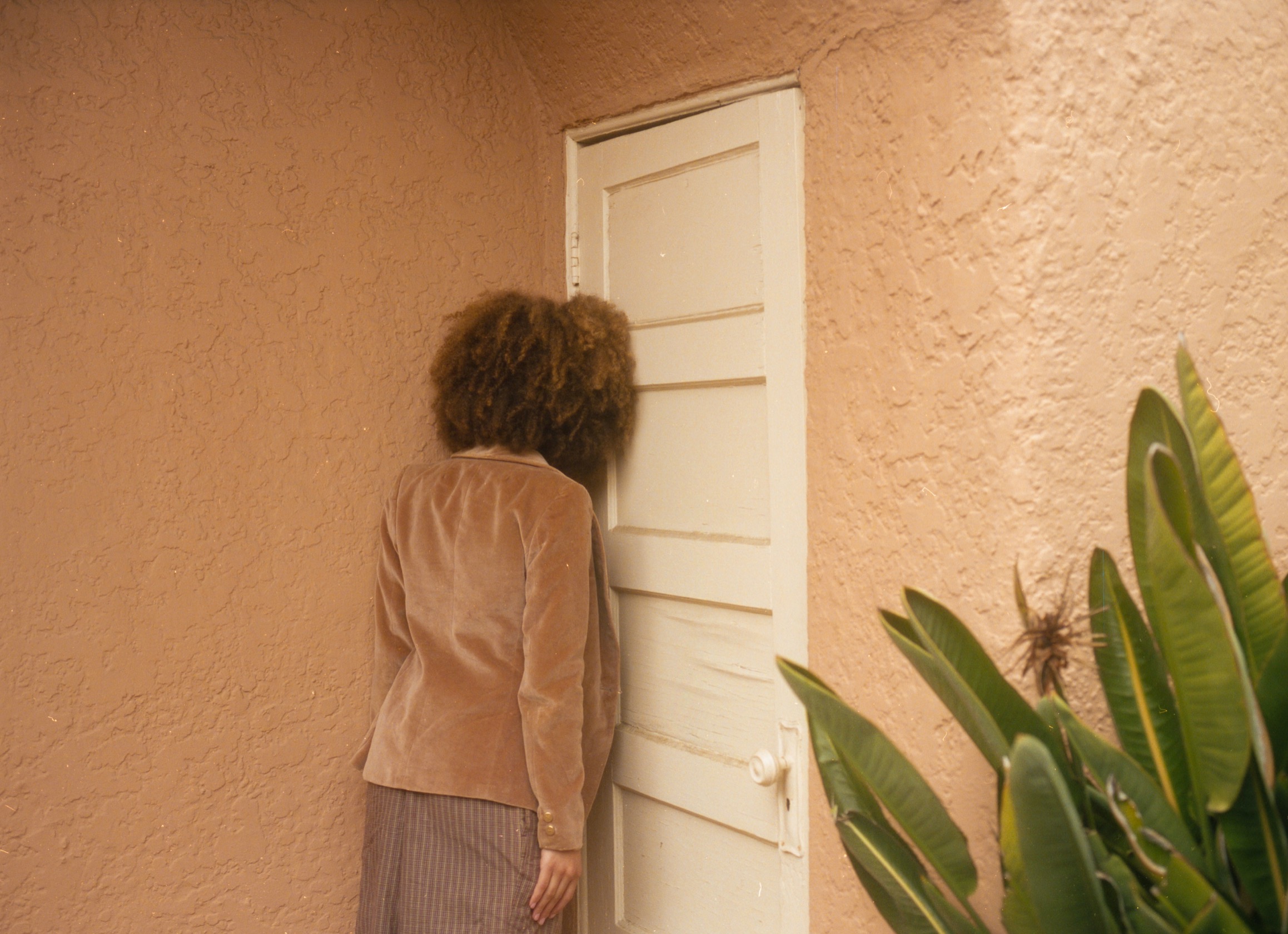 A person facing away from the camera leaning their head against a door in frustration or sadness.