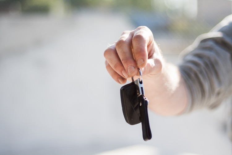 Person handing over car keys at car dealership after driver purchased insurance for a new car