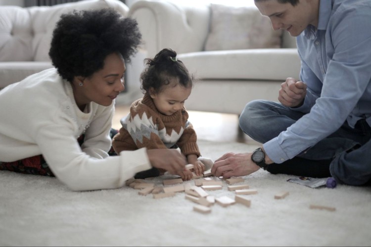 A happy couple playing jenga with their young child on their living room floor.