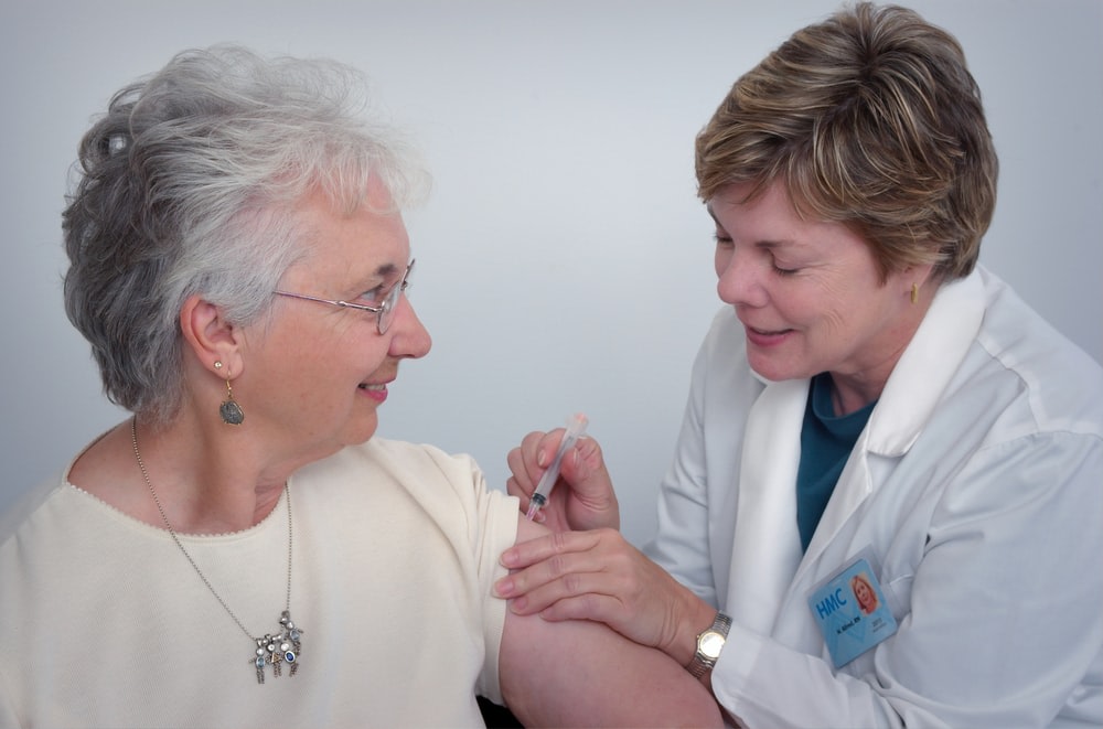 An elderly lady that is getting an injection from a nurse.