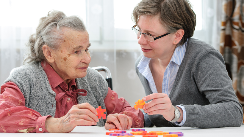 Opiekunka seniorów z seniorką układającą puzzle