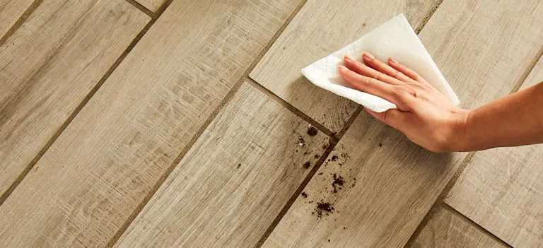 Une main de femme essuie de la saleté sur un plancher avec un essuie-tout Bounty