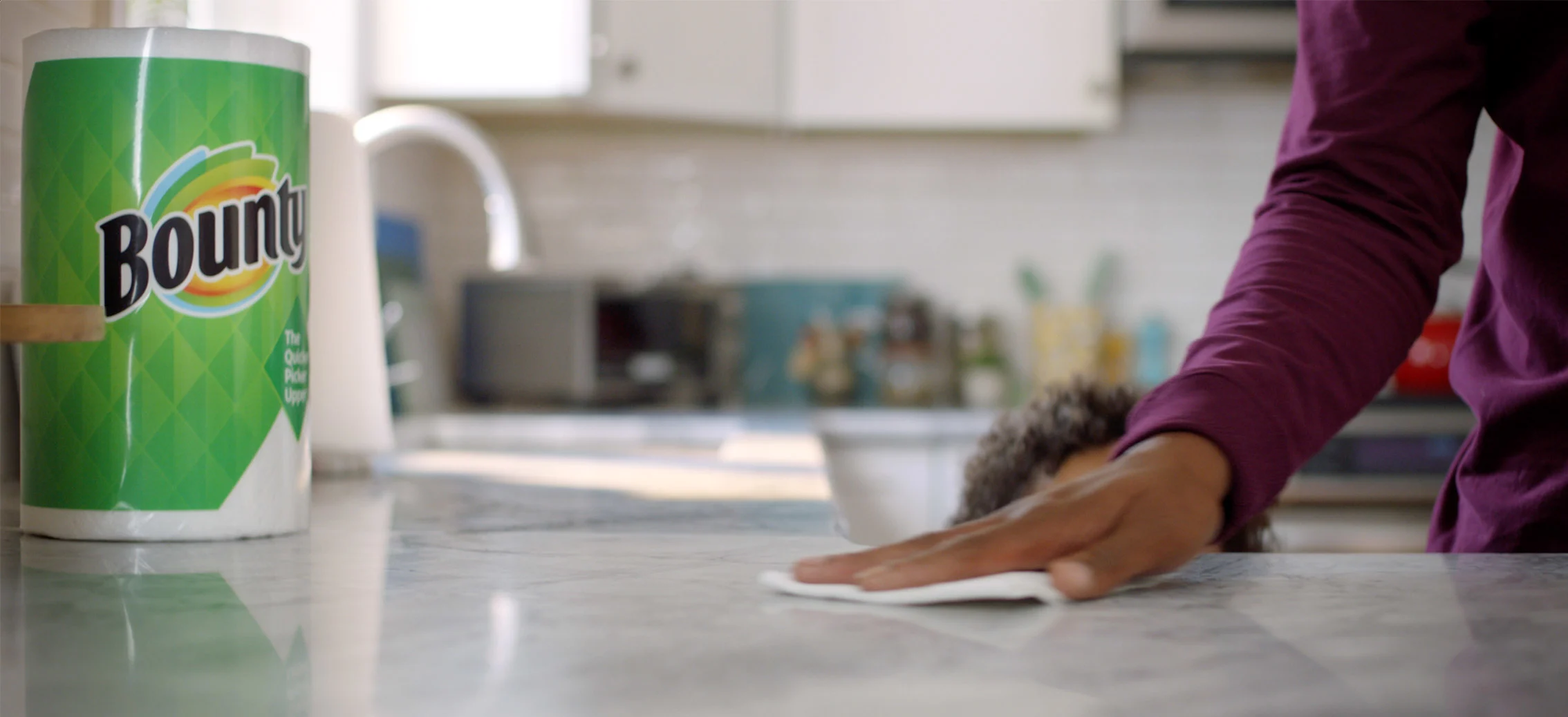 Man wiping counter with Bounty paper towel next to a Bounty paper towel roll