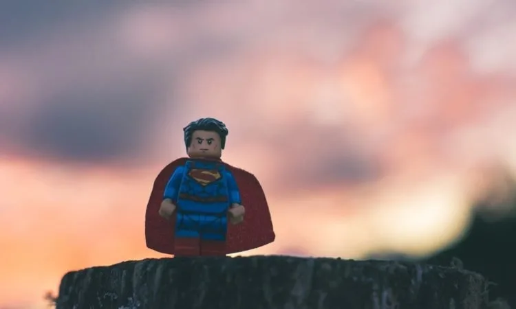 Lego Superman standing on a tree stump with a sunrise in the background.