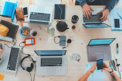 A top down view of people working on laptops at a large table.