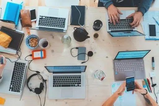 A top down view of people working on laptops at a large table.