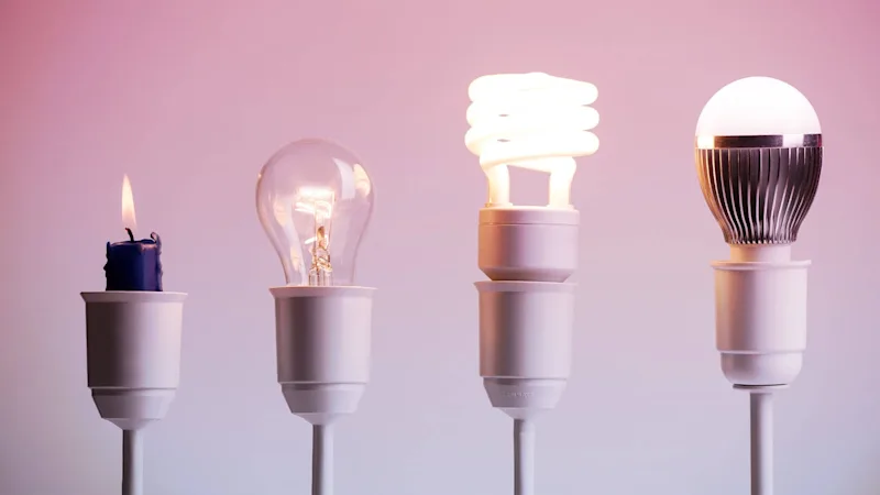 A candle next to an incandescent lightbulb, next to an led lightbulb, next to a smart lightbulb.