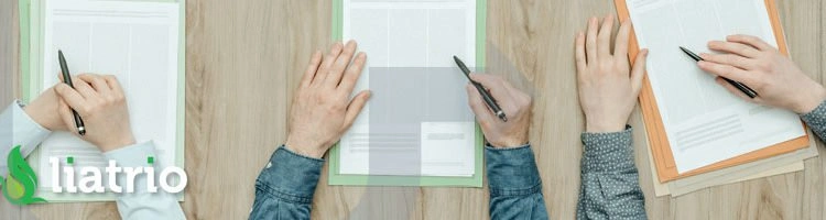 A top down view of three people writing on 3 pieces of paper on a desk.
