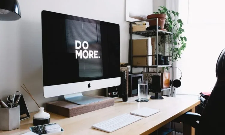 A home office desk with an iMac computer, wireless magic keyboard, and track pad, with other home office items in the background.