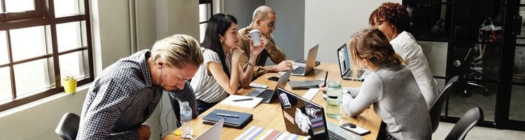 A team of 5 people working on laptops on a large table in a conference room.
