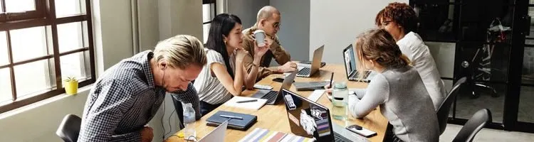 A team of 5 people working on laptops on a large table in a conference room.