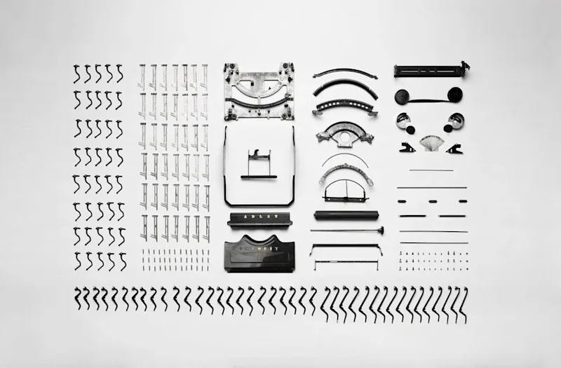 A deconstructed Adler typewriter with parts laid out in a grid.