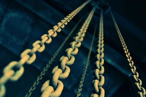 A group of industrial-sized chains attached to to a pulley in a warehouse.