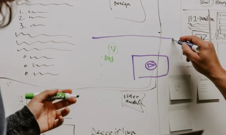 A closeup of two people diagramming on a whiteboard.