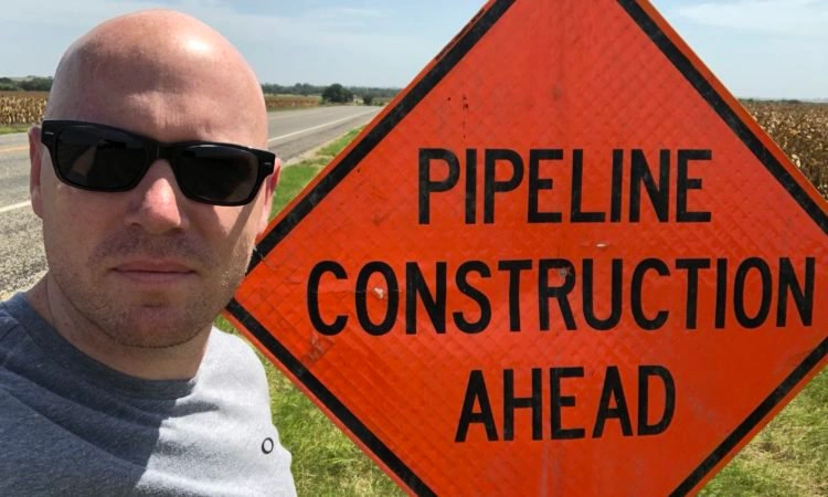 A picture of the author next to an orange construction road sign that says "Pipeline Construction Ahead".