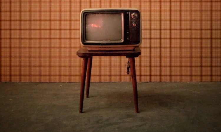 A 1950's TV sitting on a midcentury modern table in a room with olive green carpet and orange wallpaper.