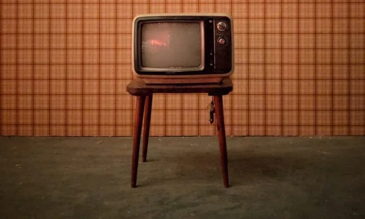 A 1950's TV sitting on a midcentury modern table in a room with olive green carpet and orange wallpaper.