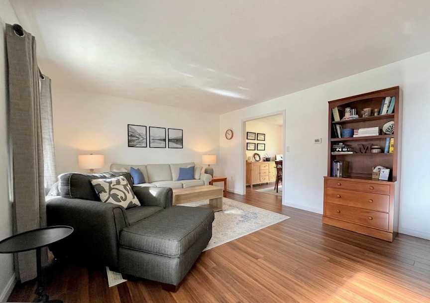 Wiltshire - Living Room - After, Removing the gas fireplace opened up the entrance way to the dining room, while replacing the carpet with hardwood flooring and softening the gray walls to an off-white brought greater warmth, brightness, and functionality to the living space.