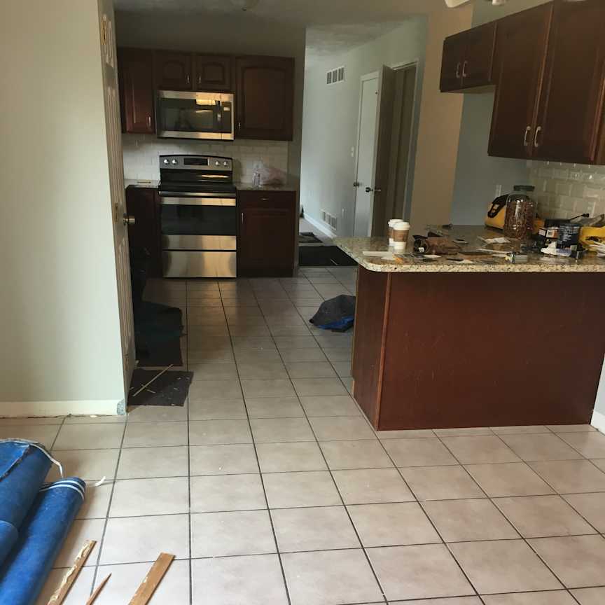 Wiltshire - Kitchen - Before, BEFORE: A floating laminate floor installed over the existing kitchen and dining room tile created awkward thresholds between the spaces, while mahogany-colored cabinets contributed to a dated, darker appearance.