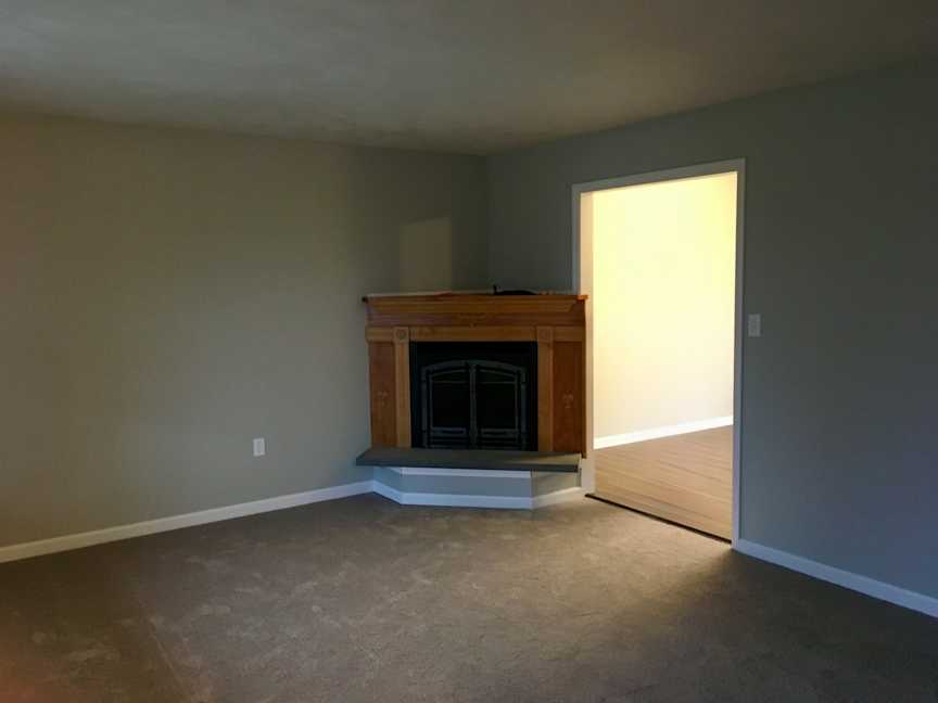 Wiltshire - Living Room - Before, BEFORE: The angled fireplace felt out of place in the living room, while the protruding hearth created an awkward obstruction between the living and dining rooms. Gray walls further contributed to the room’s dull, dark appearance.