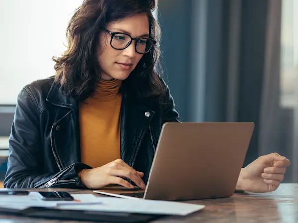 Banking professional reviewing performance data on a laptop with printed reports on the desk