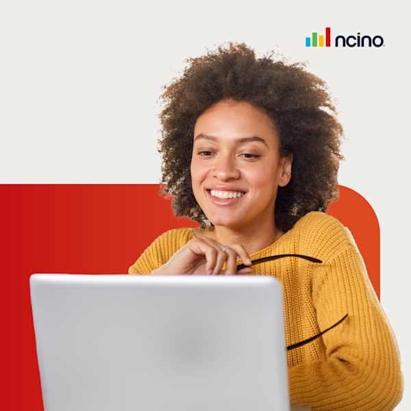A woman with a curly afro in a yellow shirt holds her glasses while smiling at a laptop.