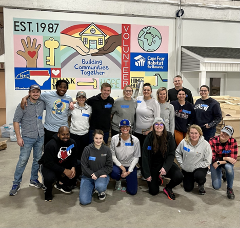 nCino employees volunteer at Habitat for Humanity and pose in front of Habitat for Humanity sign.