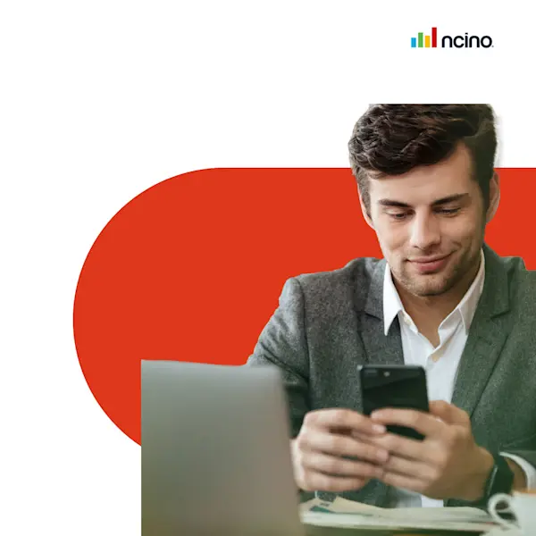 A man who is learning the value or credit portfolio management and credit risk management views his phone in front of his laptop against a red backdrop.
