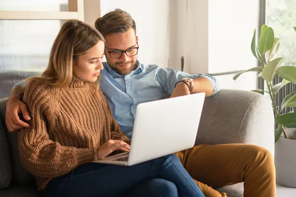 A couple sitting together on a couch using a laptop at home.