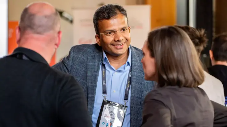 Three happy, professional-looking individuals wearing Money2020 delegate badges, engaged in conversation.