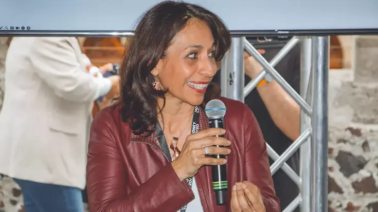 A woman holding a microphone, wearing a Money2020 delegate badge, speaking a meet-up