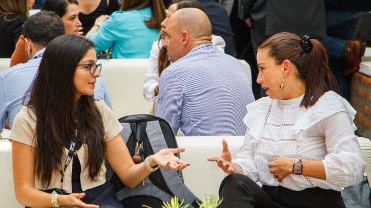 Two professional women in a crowd, having an in-depth conversation, surrounded by engaged people networking.