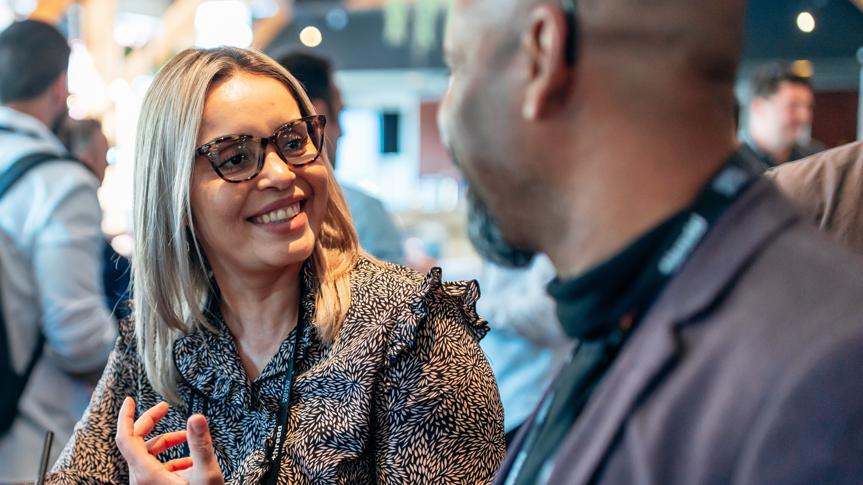 Two professionals in a crowd, having an in-depth conversation, surrounded by engaged people networking.