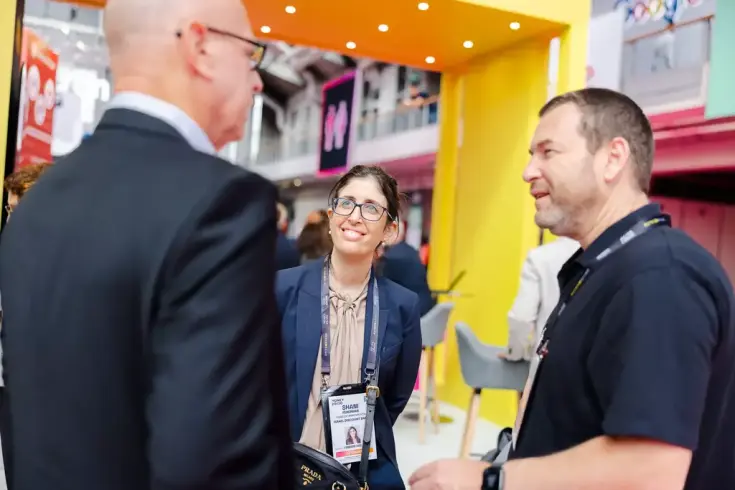 Three happy, professional-looking individuals wearing Money2020 delegate badges, engaged in conversation.