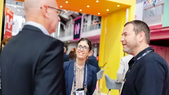 Three happy, professional-looking individuals wearing Money2020 delegate badges, engaged in conversation.