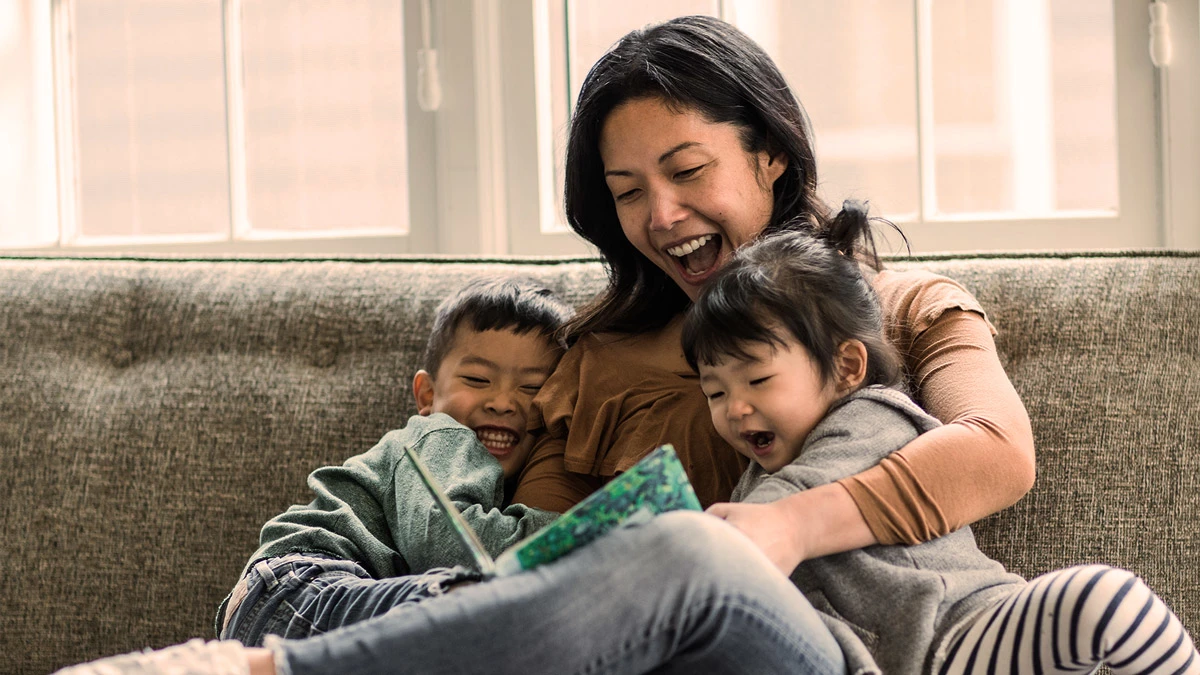 Mother and two children sitting on a couch reading a book