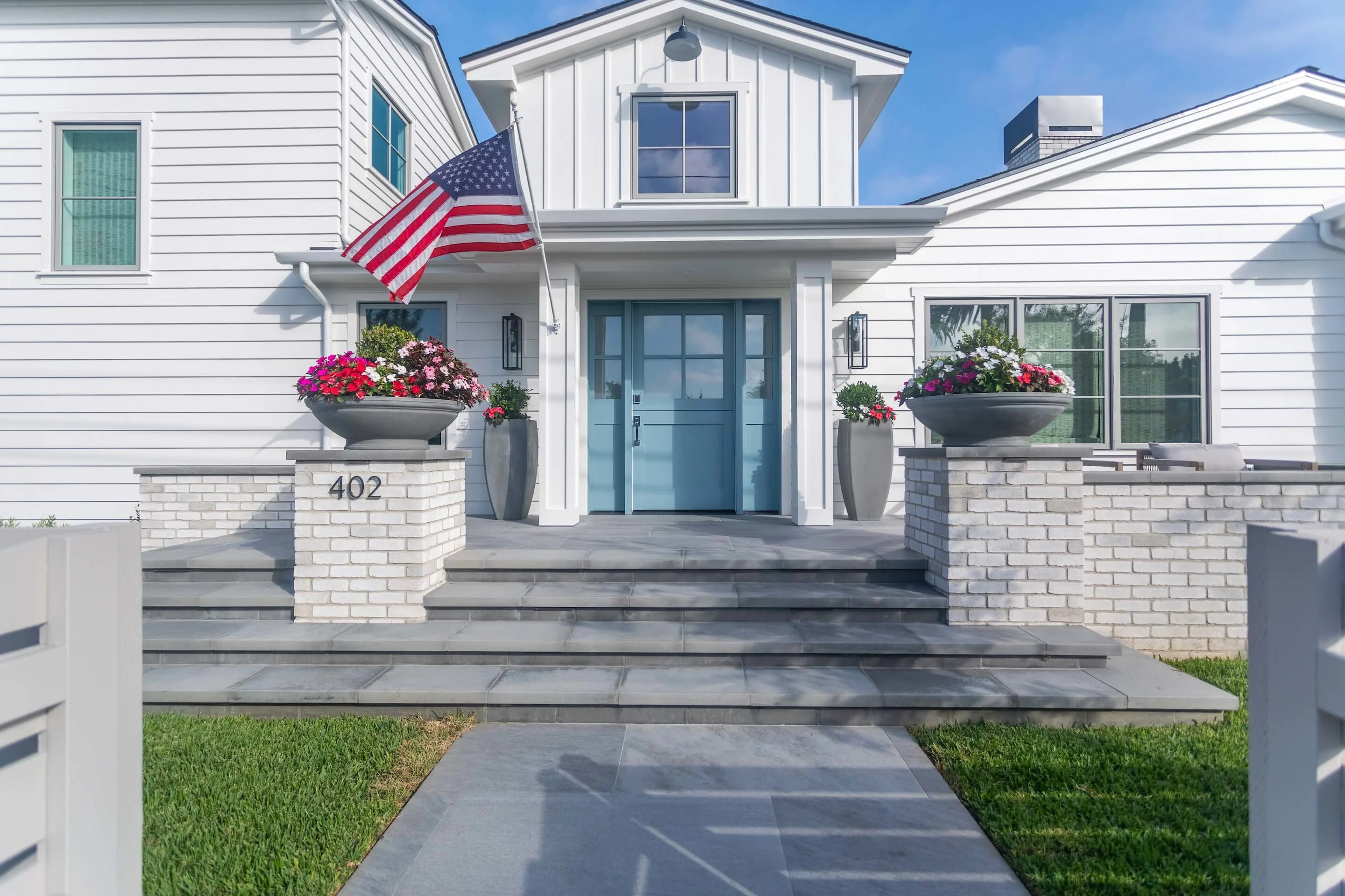 Modern Southern California home with sweeping paver steps entry, stone pillars, paver walkway, and waving flag