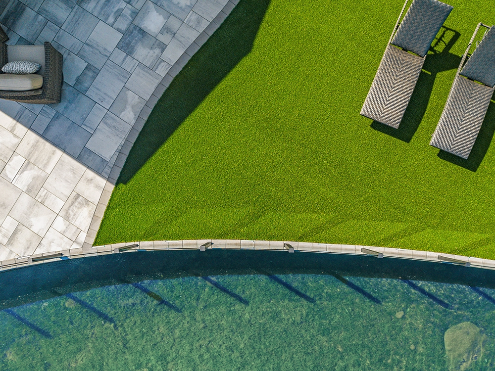 Artificial grass and paver patio next to water. 