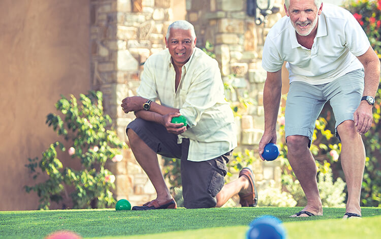Two older men, one white and one black, playing bocce on a turf lawn
