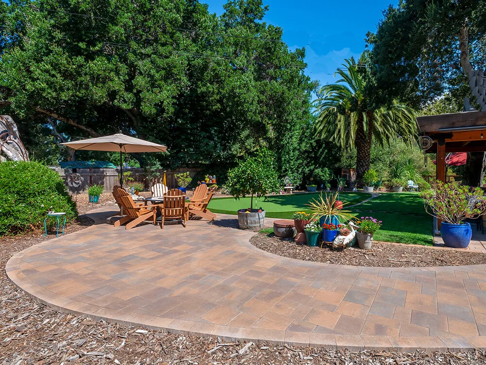Cobblestone patio with turf and planters. Umbrella with chairs. 