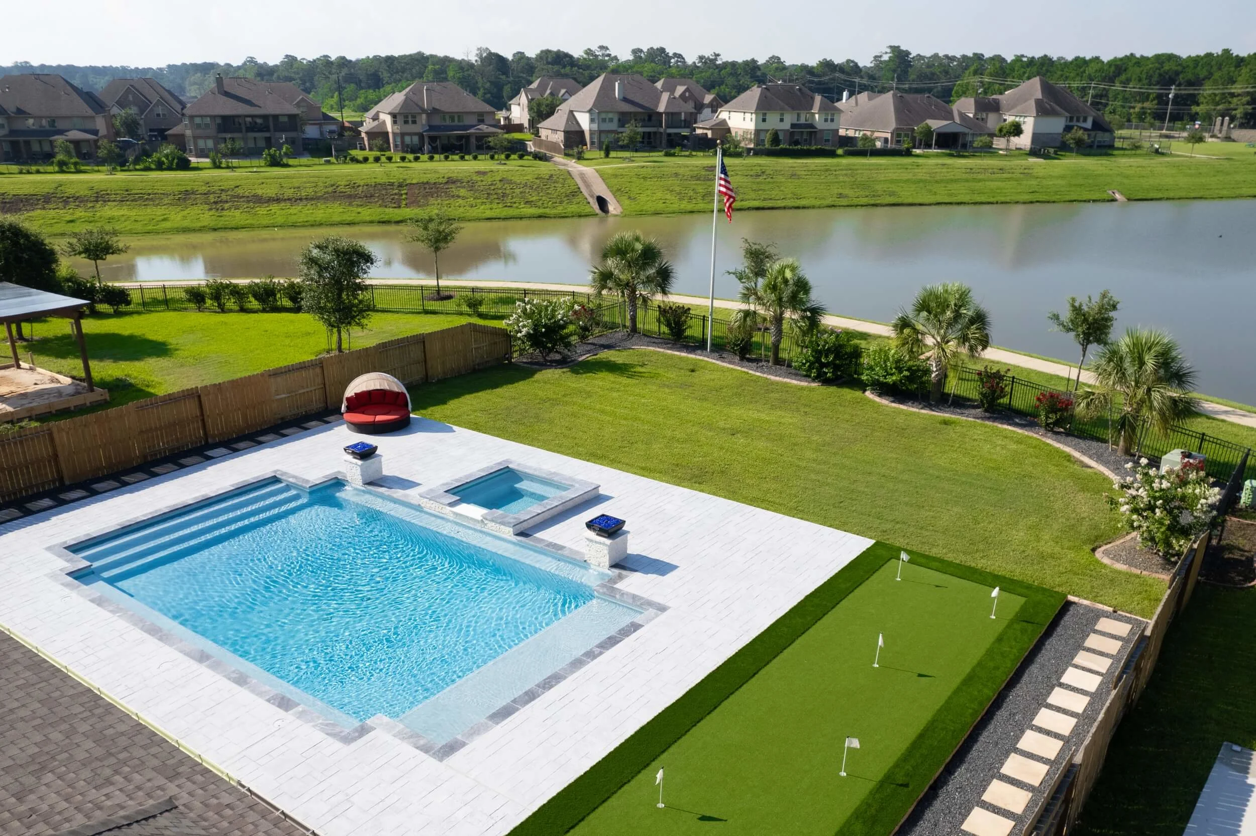 Aerial overview of Houston backyard remodel with poolside turf putting green and paver walkways by a lake