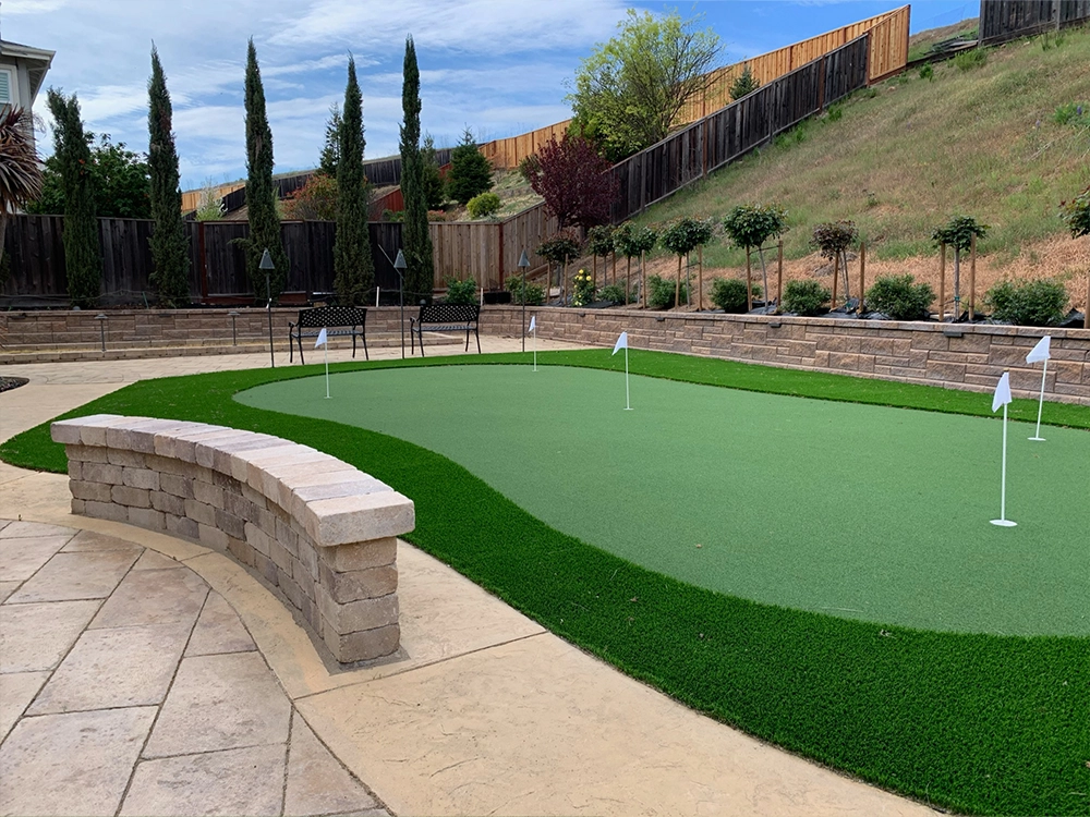 Backyard putting green by paving stone patio. 